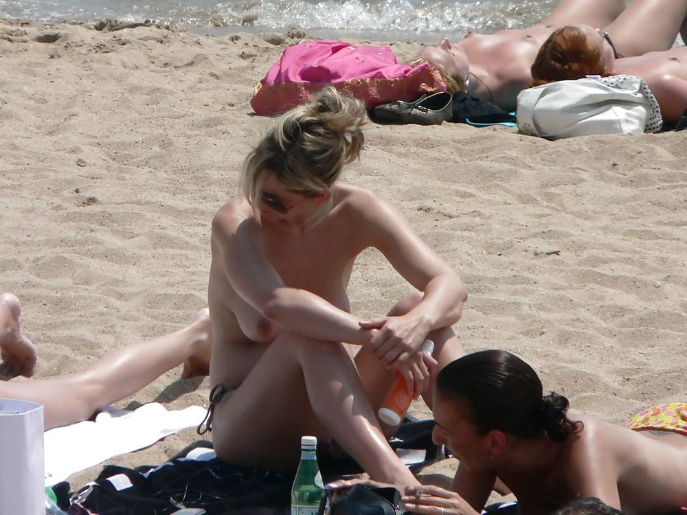 金髪の女性が浜辺で着替えている姿は、トップレスの恋人たちのためのものです。
 #97316204